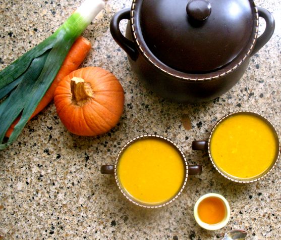 Overhead view of 2 servings pumpkin carrot curry soup surrounded by serving bowl and vegetables